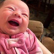 Blakely joined the competition — help win amazing prizes! baby, newborn, infant, smiling, laughing, face, onesie, pink_clothing, heart_pattern, button, arm, bracelet, couch, chair, home_interior, blurred_background, portrait, close_up, happy, cute