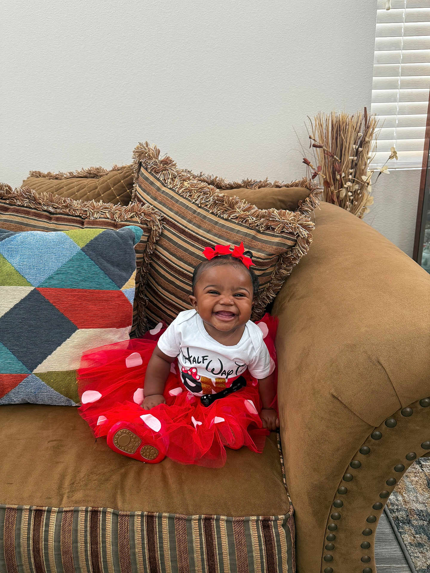 Carmyn joined the competition — help win amazing prizes! baby, smiling, tutu, red_bow, couch, pillow, indoor, child, happy, sitting, clothing, footwear, decor, window_blinds, home_interior, person, cute, infant, fashion, portrait