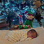 Amari-Alexander joined the competition — help win amazing prizes! baby, newborn, sleeping, blanket, christmas_tree, holiday, decorations, lights, elf_doll, toy, festive, cozy, soft, indoors, wooden_floor, present, pajamas, child, cute, peaceful
