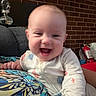 baby, brick_wall, child, colorful, cozy, cushion, cute, face, fire_extinguisher, hand, happy, head, indoor, infant, joyful, onesie, patterned, person, portrait, smiling