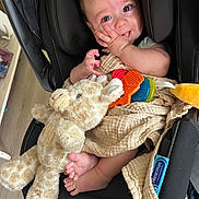 Arlus is registered to the contest to win money with this photo: baby, infant, car_seat, plush_toy, giraffe, teething_toys, blanket, hand, feet, cute, child, person, indoors, smiling, happy, soft_toy, fabric, comfort, seat, closeup