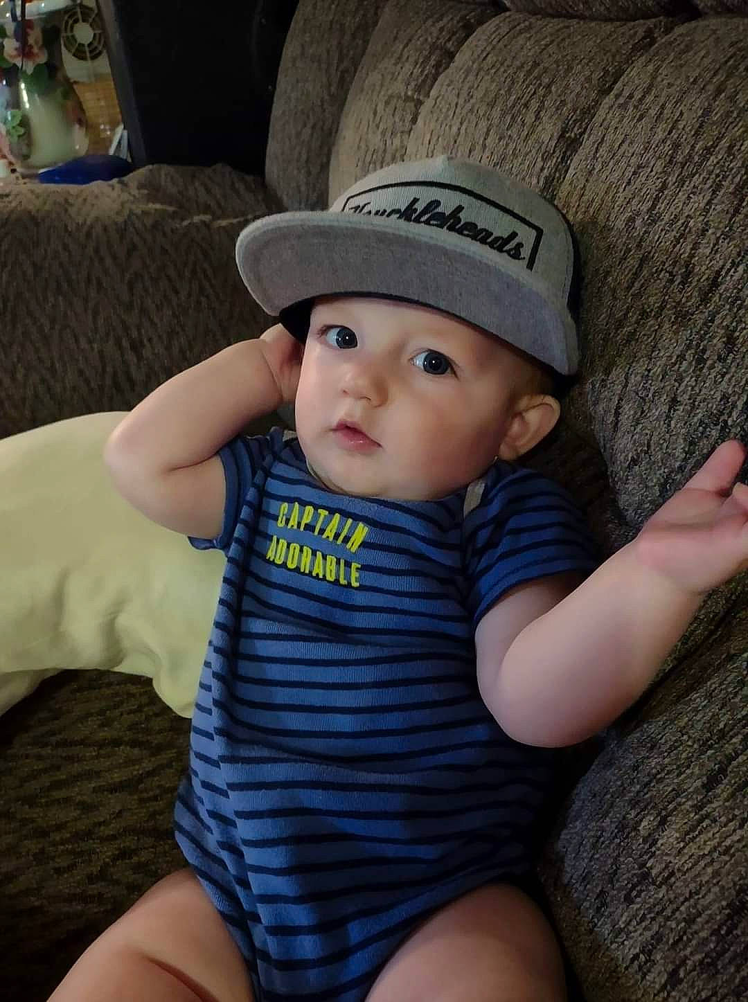 Charlie is registered to the contest to win money with this photo: arm, baby, baby_toddler_clothing, cap, cheek, child, comfort, couch, fashion_accessory, flash_photography, hat, headgear, headwear, human_leg, lip, person, sitting, skin, smile, sun_hat
