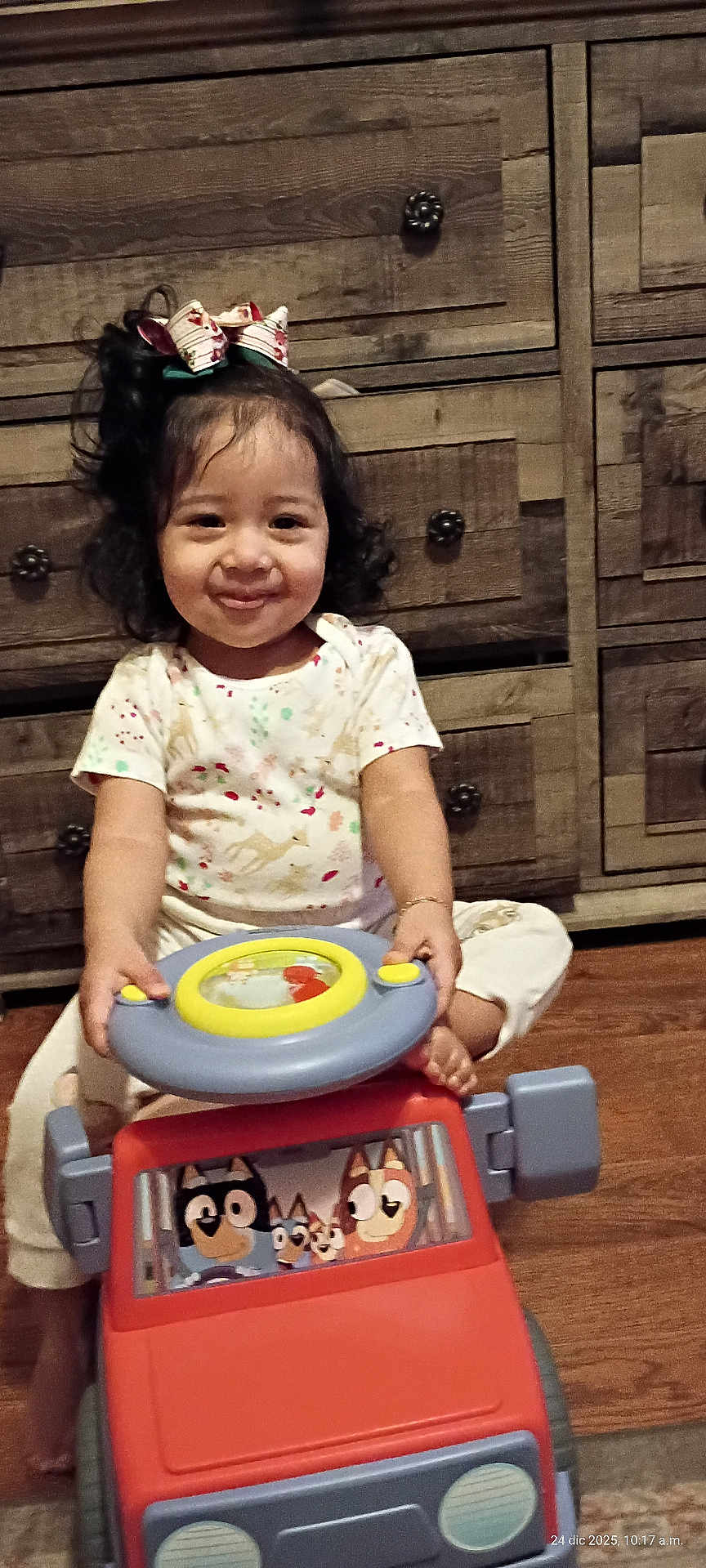 Alisson Abril joined the competition — help win amazing prizes! child, toddler, smile, toy_car, steering_wheel, bow, curly_hair, pajamas, sitting, wooden_dresser, drawer_knobs, hardwood_floor, indoor, portrait, play, hands, feet, happy, camera, cute