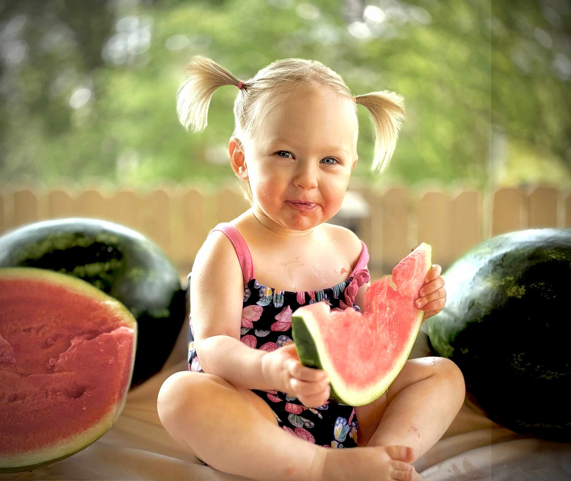 Liala joined the competition — help win amazing prizes! child, toddler, watermelon, fruit, summer, outdoor, pigtails, eating, happy, cute, sitting, food, snack, playful, nature, greenery, fence, daylight, portrait, smiling