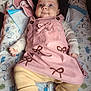 baby, infant, pink_dress, bows, beige_pants, ribbed_clothing, long_sleeve, lying_down, baby_mat, patterned_mat, blue_eyes, curious_expression, soft_blanket, pacifier, comfortable, cute, child, indoors, clothing, portrait