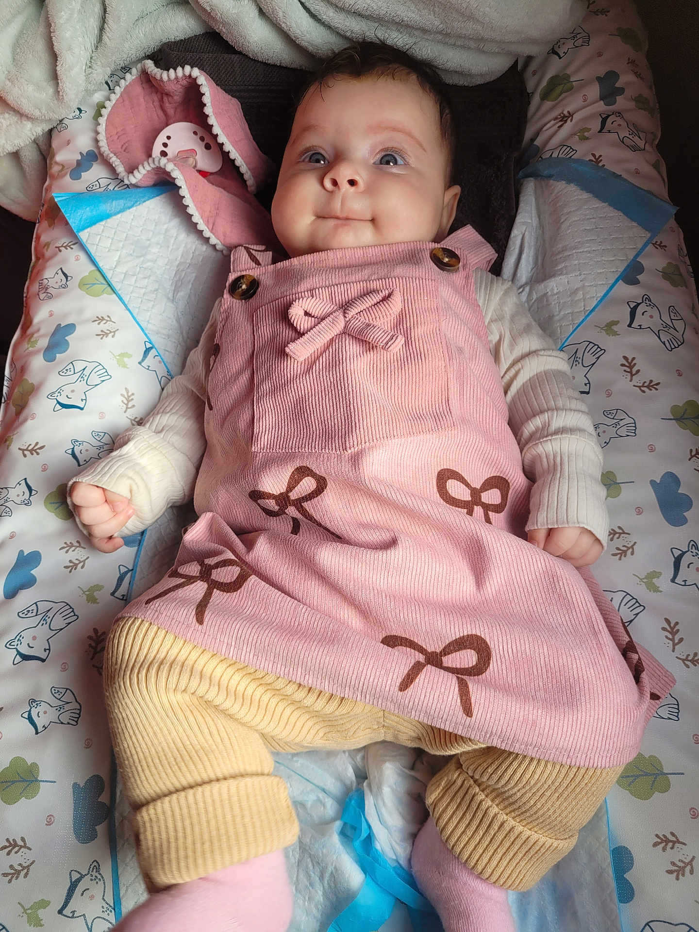 Rosalie a rejoint le concours — aidez-le/la à gagner de superbes lots ! baby, infant, pink_dress, bows, beige_pants, ribbed_clothing, long_sleeve, lying_down, baby_mat, patterned_mat, blue_eyes, curious_expression, soft_blanket, pacifier, comfortable, cute, child, indoors, clothing, portrait