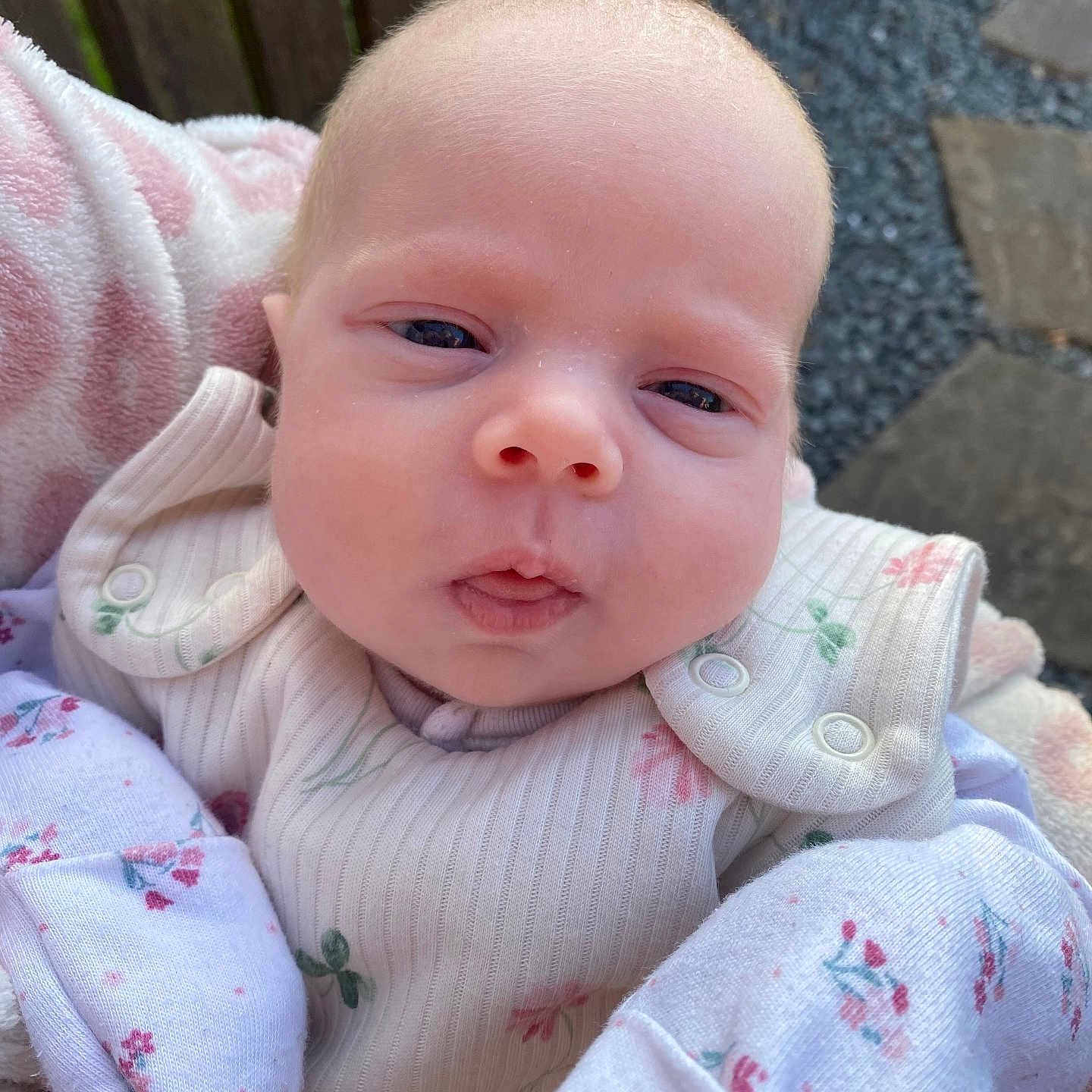 Louella-Mae joined the competition — help win amazing prizes! baby, blanket, close_up, clothing, curious_expression, cute, face, floral_pattern, infant, natural_light, newborn, outdoor, pale_skin, portrait, resting, small_hands, soft_texture, stone, wood, wrapped