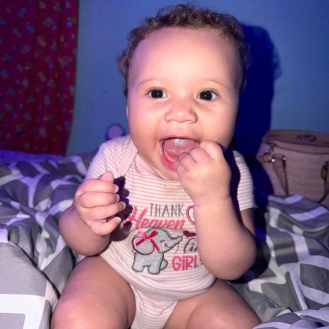 Samiyah joined the competition — help win amazing prizes! baby, child, infant, sitting, smiling, happy, face, curly_hair, hand, finger, bed, bedroom, blanket, bedspread, striped_clothing, onesie, plush_toy, indoor, portrait, flash_photography