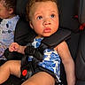 baby, child, infant, car_seat, seatbelt,  안전, portrait, wide_eyed, curly_hair, sitting, vehicle, backseat, travel, floral_clothing, toy, red_buckle, second_child, indoors, close_up, family