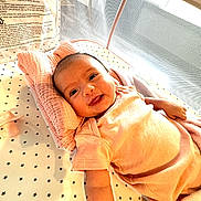 Hadley joined the competition — help win amazing prizes! baby, smiling, infant, crib, pillow, blanket, star_pattern, mesh, natural_light, sleeping_area, child, cute, happy, soft_fabric, lying_down, indoors, newborn, pink_clothing, pacifier, comfort
