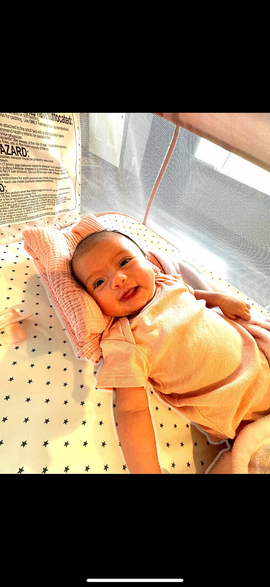 Hadley joined the competition — help win amazing prizes! baby, smiling, infant, crib, pillow, blanket, star_pattern, mesh, natural_light, sleeping_area, child, cute, happy, soft_fabric, lying_down, indoors, newborn, pink_clothing, pacifier, comfort
