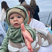 Izayah joined the competition — help win amazing prizes! toddler, child, baby, hoodie, beanie, blanket, hand, ocean, boat, water, person, adult, sky, cloudy, outdoor, casual_clothing, portrait, expression, reaching, people