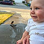 baby, child, smiling, face, hand, person, ducks, bird, animal, outdoor, daylight, driveway, suburb, house, grass, clothing, white_shirt, holding, happy, nature