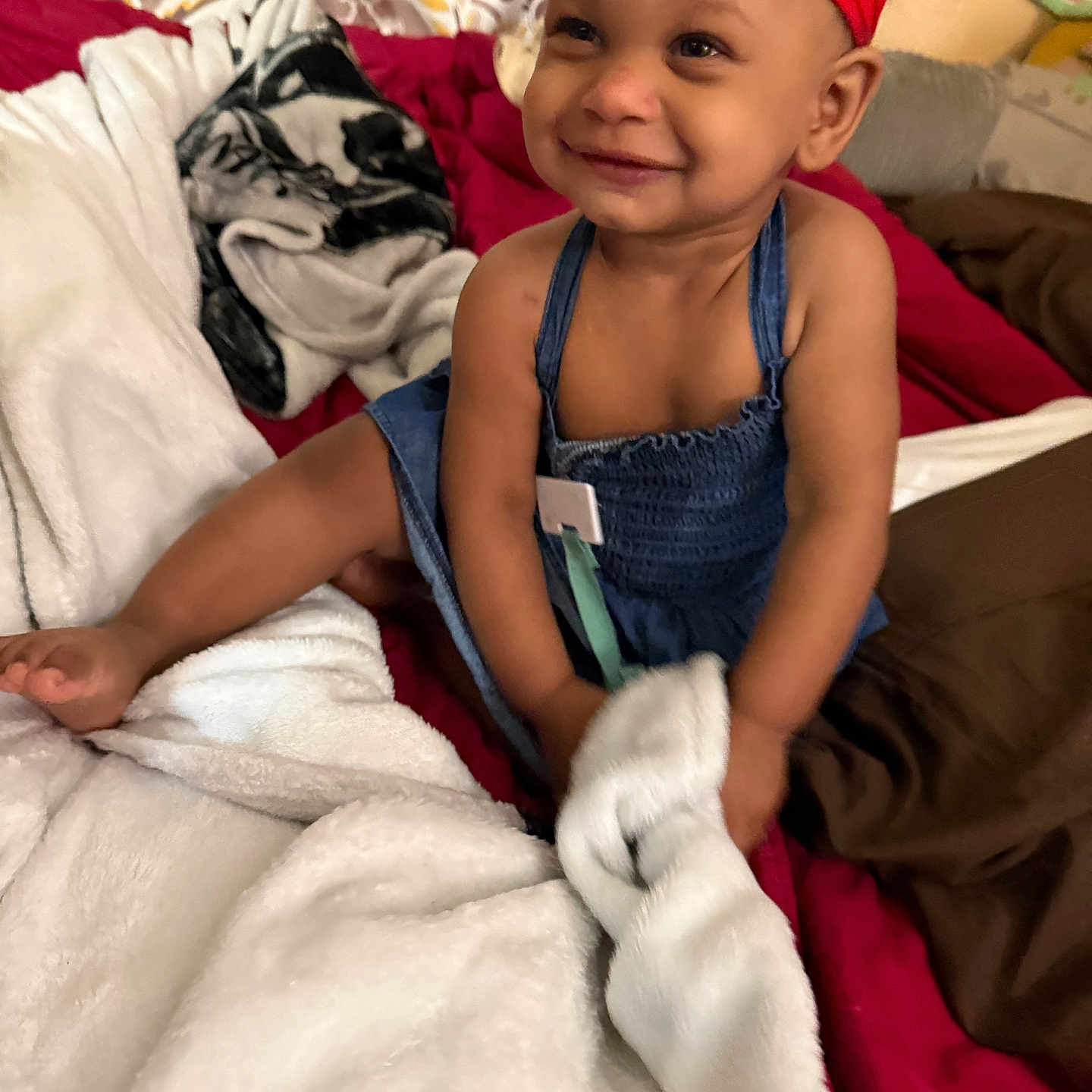 Annalise is registered to the contest to win money with this photo: toddler, child, smile, red_headband, blue_dress, blanket, bed, happy, indoors, person, face, skin, foot, hand, fabric, pattern, comfort, cozy, cute, portrait