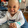 Annalise is registered to the contest to win money with this photo: baby, child, smiling, face, bow, clothing, nike, shirt, sitting, indoor, bed, blanket, toy, pacifier, hand, fan, floor, curly_hair, person, happy