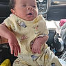 baby, infant, child, portrait, sitting, car, vehicle, backseat, dashboard, yellow_outfit, cartoon_print, onesie, newborn, face, hands, eyes, indoor, daylight, family, cute