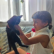 Rose participe au concours pour gagner de l'argent avec cette photo : child, girl, black_cat, pet, indoor, window, curtain, sunlight, braids, sweater, red_shorts, polka_dots, holding, face, animal, furniture, couch, expression, portrait, home