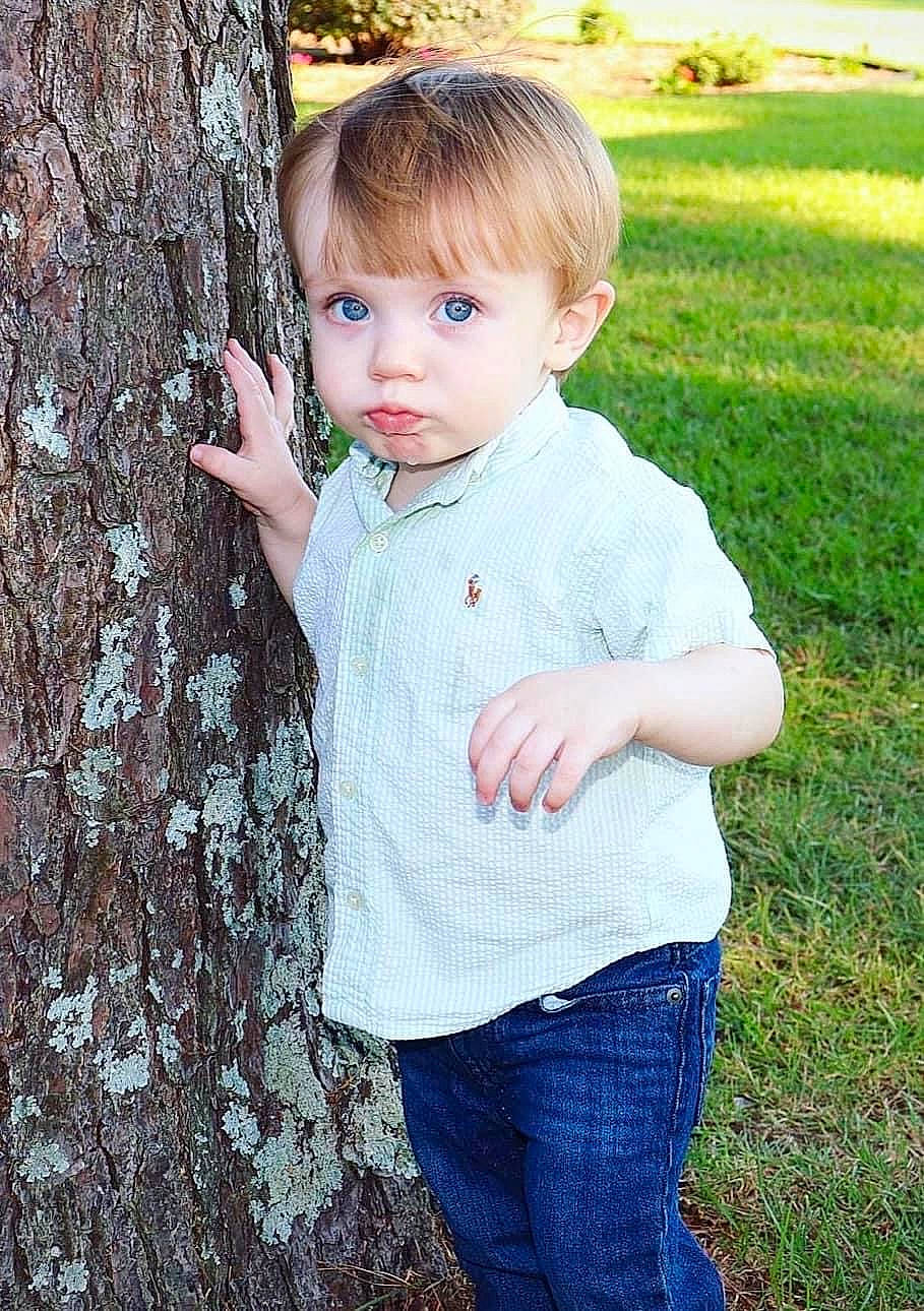 Grayson is registered to the contest to win money with this photo: baby_toddler_clothing, cool, face, gesture, grass, hair, hairstyle, hand, happy, head, jeans, lip, people_in_nature, person, photograph, plant, skin, sleeve, toddler, tree