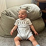baby, child, smiling, sitting, carpet, bean_bag, indoor, white_clothing, socks, wooden_furniture, curtain, tassel, happy, person, floor, cute, infant, cozy, home, portrait