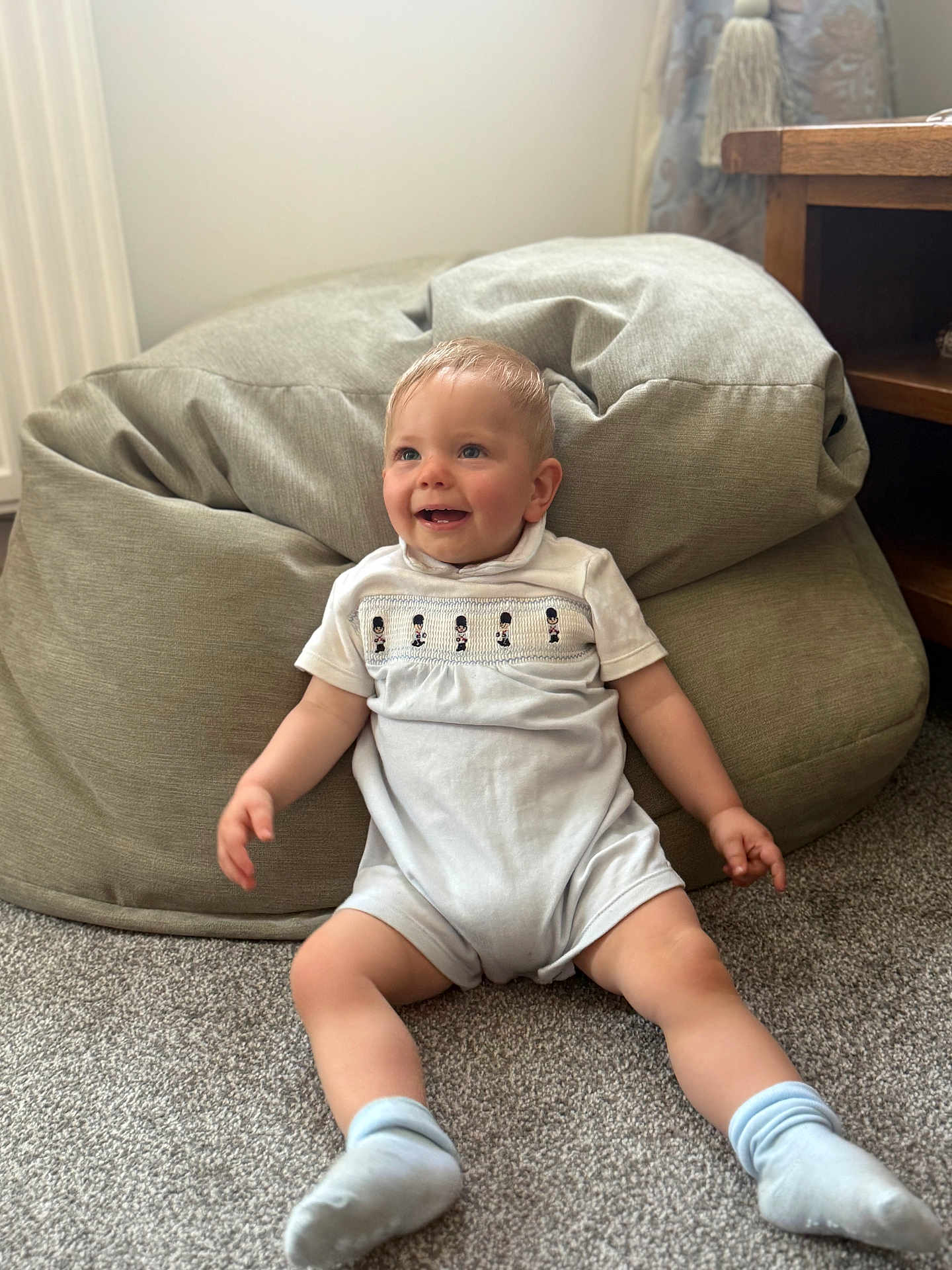 Jack joined the competition — help win amazing prizes! baby, child, smiling, sitting, carpet, bean_bag, indoor, white_clothing, socks, wooden_furniture, curtain, tassel, happy, person, floor, cute, infant, cozy, home, portrait