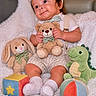 baby, child, teddy_bear, plush_toy, stuffed_animal, bunny, dinosaur, soft_toy, colorful_block, colorful_ball, cap, bowtie, white_socks, striped_shorts, white_shirt, blanket, smiling, sitting, indoors, cute