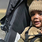 Presley is registered to the contest to win money with this photo: baby, child, stroller, hat, knit_hat, bear_design, face, eyes, clothing, straps, seat, infant, cute, portrait, indoor, expression, young_child, warm_clothing, black_stroller, closeup
