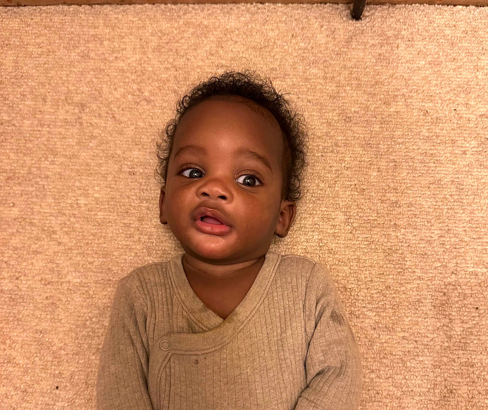 Presley joined the competition — help win amazing prizes! child, toddler, baby, face, eyes, curly_hair, beige, carpet, clothing, ribbed, expression, portrait, indoor, laying_down, curious, young, person, skin, head, casual