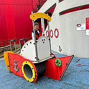 Nill participe au concours pour gagner de l'argent avec cette photo : child, playground, play_structure, ship, red, yellow, blue, curly_hair, smiling, outdoor, urban, concrete_wall, railings, play_equipment, person, happy, daylight, fun, recreation, young
