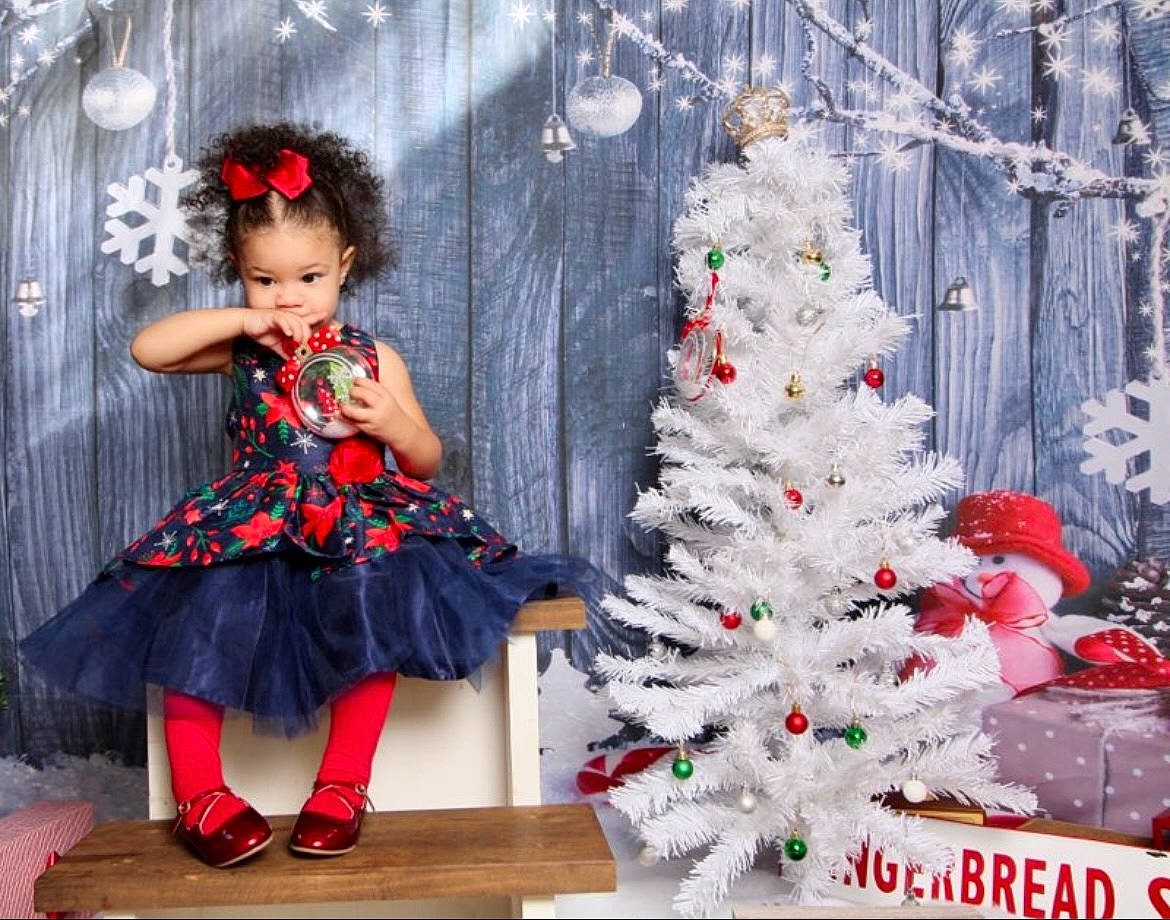 Story is registered to the contest to win money with this photo: baby_toddler_clothing, christmas_decoration, christmas_ornament, christmas_tree, day_dress, dress, event, evergreen, fashion_design, hat, holiday_ornament, human_body, leaf, ornament, person, pink, plant, red, standing, toddler