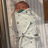 Hailey is registered to the contest to win money with this photo: newborn, baby, swaddle, pacifier, hospital, bassinet, sleeping, infant, blanket, space_theme, stars, planets, cute, wrapped, bed, striped_sheet, soft, peaceful, indoors, person