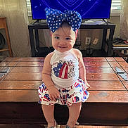 Adeline joined the competition — help win amazing prizes! toddler, child, smiling, indoor, wooden_chest, television, blue_bow, patriotic_clothing, sandals, floor, curtains, living_room, happy, 4th_of_july, american_flag_pattern, headband, person, furniture, heart_pattern, casual