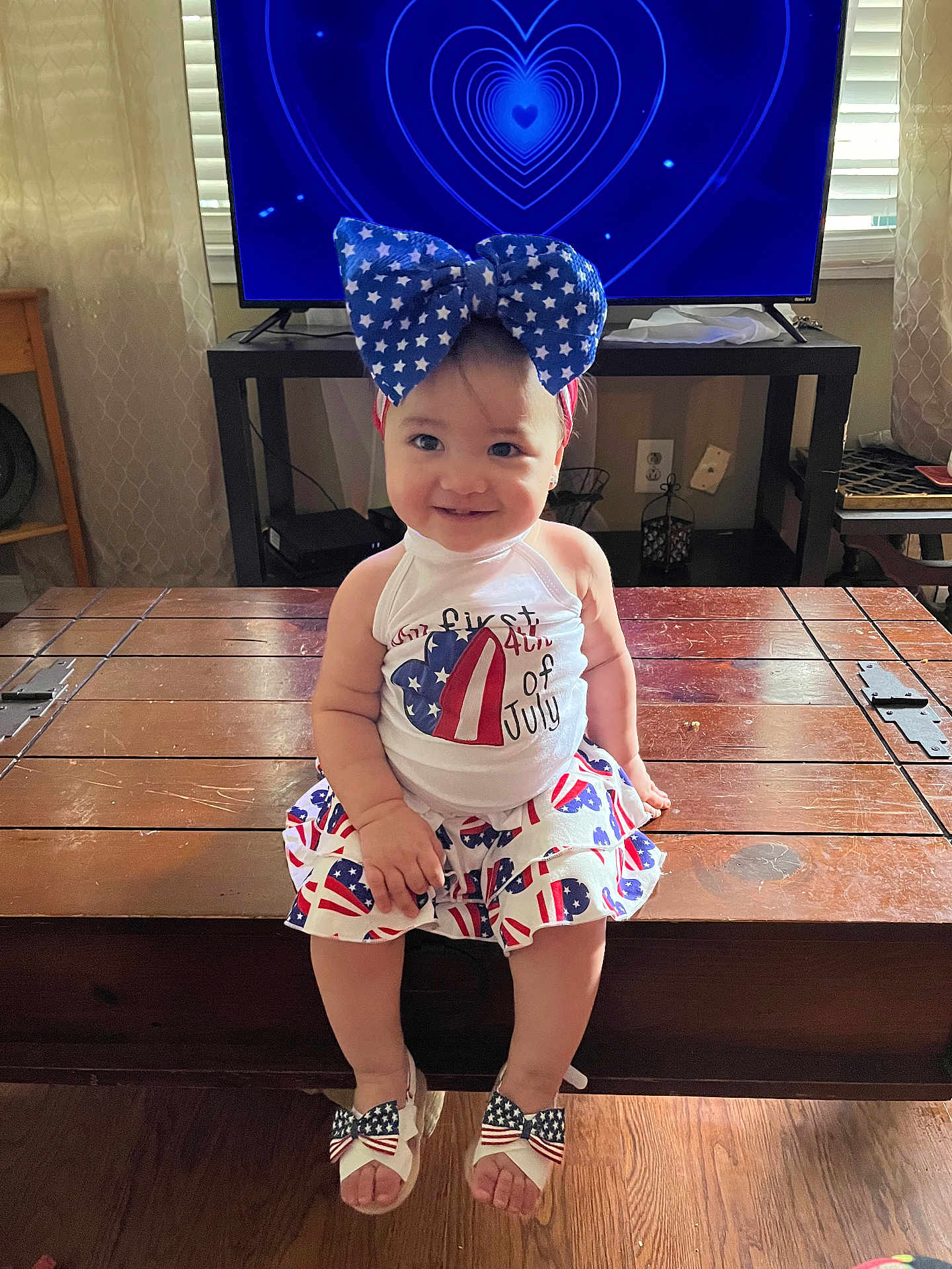 Adeline joined the competition — help win amazing prizes! toddler, child, smiling, indoor, wooden_chest, television, blue_bow, patriotic_clothing, sandals, floor, curtains, living_room, happy, 4th_of_july, american_flag_pattern, headband, person, furniture, heart_pattern, casual