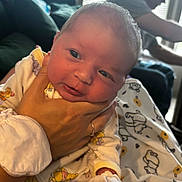 Adaline joined the competition — help win amazing prizes! baby, newborn, hand, onesie, infant, person, adult, bed, blanket, cartoon_print, indoor, window, cap, blurred_background, face, portrait, caring, soft_lighting, family, resting