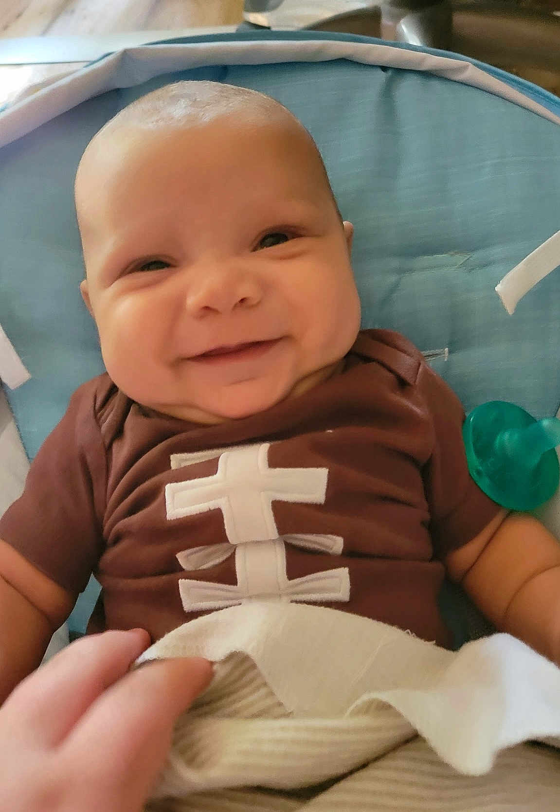 Jackson is registered to the contest to win money with this photo: baby, smiling, infant, brown_shirt, blue_cushion, pacifier, hand, blanket, cute, happy, face, portrait, child, indoor, closeup, person, seat, comfort, skin, expression