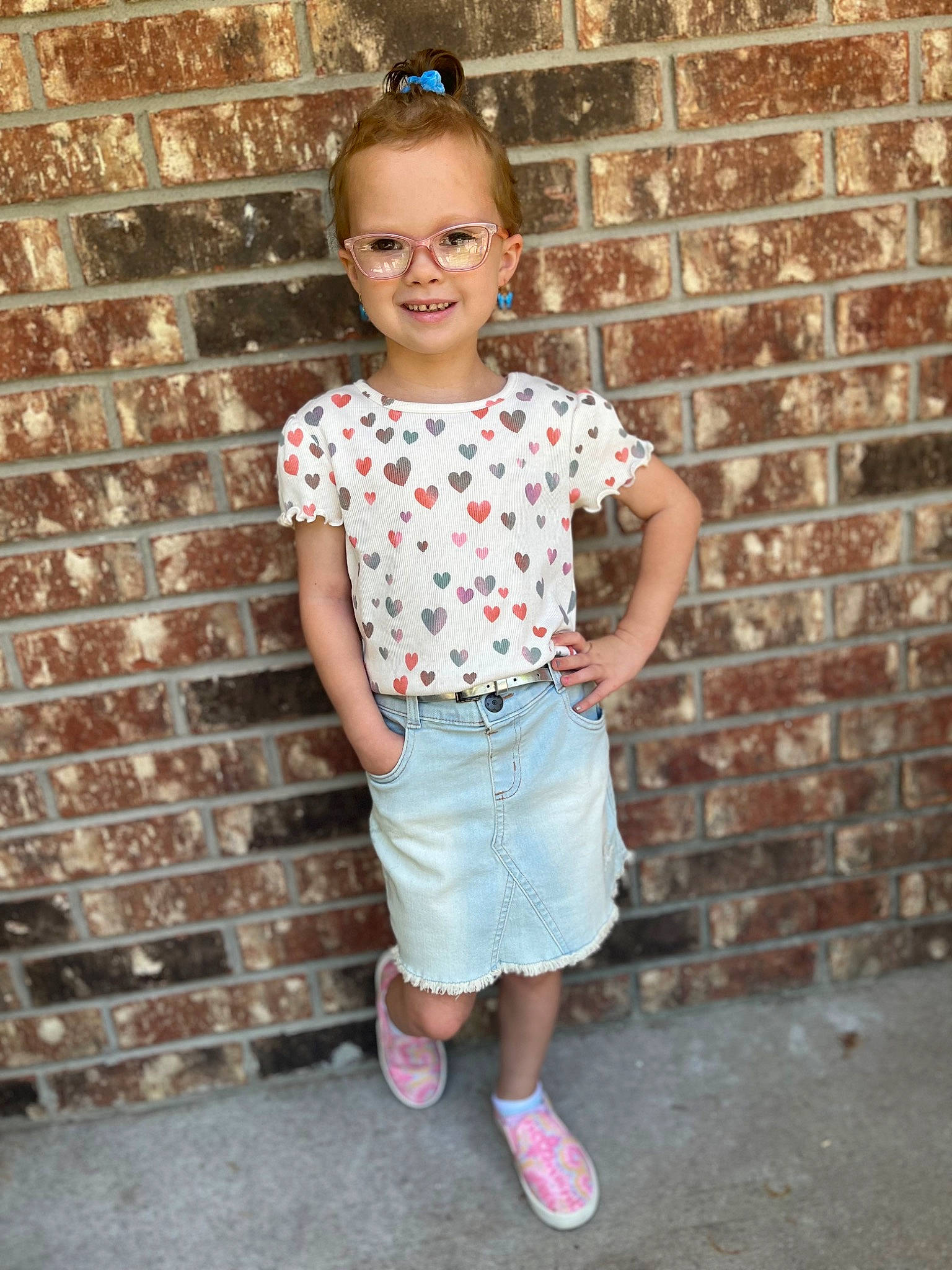 Peighton is registered to the contest to win money with this photo: baby_toddler_clothing, brick, clothing, denim, facial_expression, glasses, happy, human_body, joy, neck, person, pink, plaid, shorts, sleeve, smile, standing, street_fashion, t_shirt, thigh