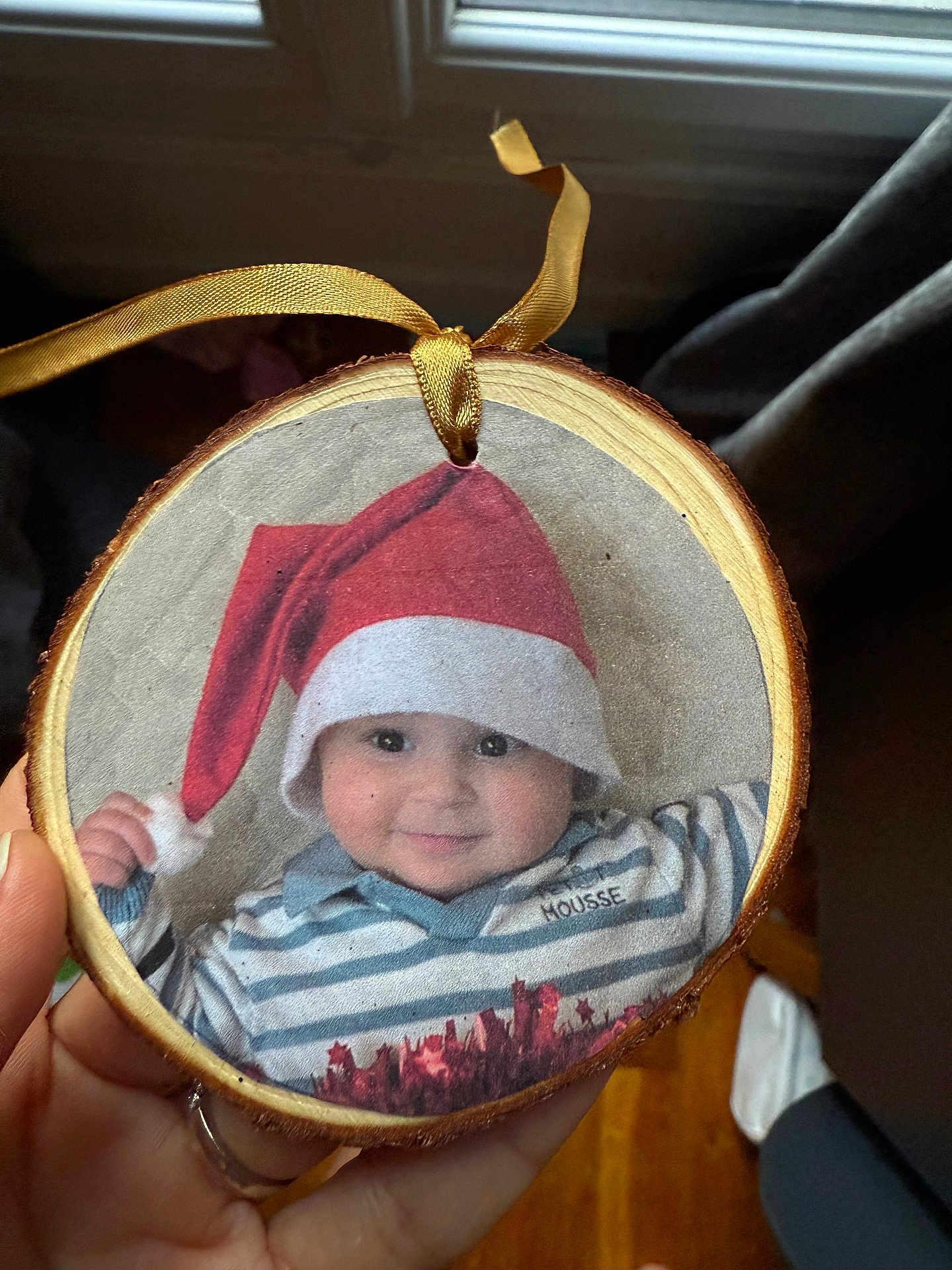 Côme a rejoint le concours — aidez-le/la à gagner de superbes lots ! baby, child, santa_hat, striped_shirt, wooden_ornament, hand, face, smile, indoors, ribbon, holiday, christmas, portrait, cute, person, decor, holding, window, wood, seasonal
