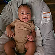 August is registered to the contest to win money with this photo: baby, infant, smiling, onesie, socks, baby_seat, cushion, happy, child, indoor, person, cute, skin, face, small_hands, small_feet, wood_floor, comfort, relaxing, portrait