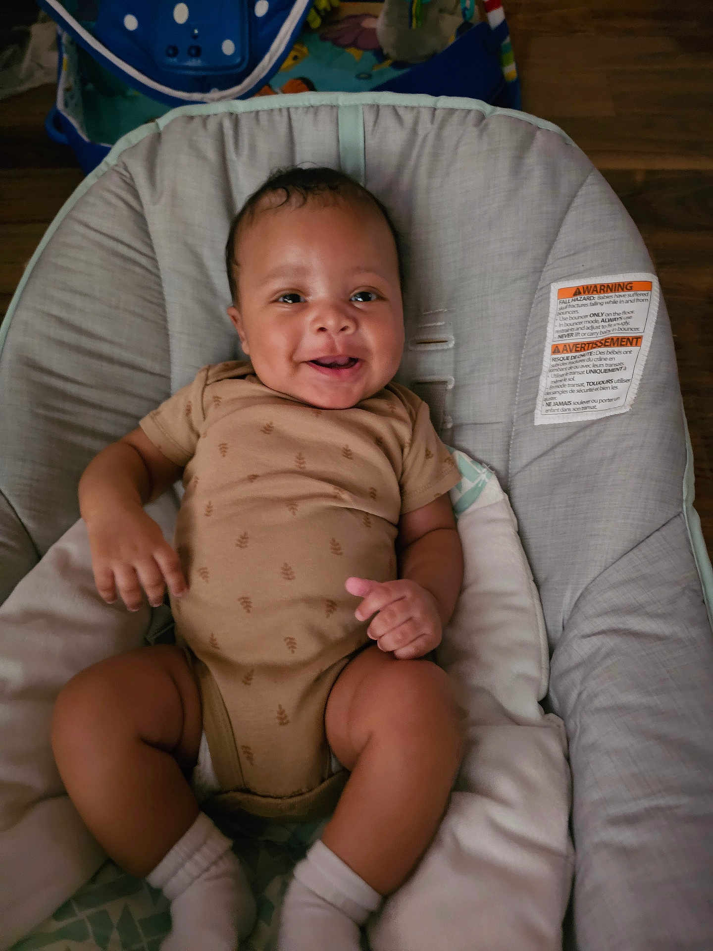 August is registered to the contest to win money with this photo: baby, infant, smiling, onesie, socks, baby_seat, cushion, happy, child, indoor, person, cute, skin, face, small_hands, small_feet, wood_floor, comfort, relaxing, portrait