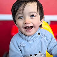 Aiden a rejoint le concours — aidez-le/la à gagner de superbes lots ! child, toddler, smiling, happy, face, sweater, cat_design, blue_sweater, play_area, toy_steering_wheel, indoor, short_hair, cute, young_child, portrait, bright_colors, red_background, yellow_background, closeup, person
