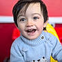 child, toddler, smiling, happy, face, sweater, cat_design, blue_sweater, play_area, toy_steering_wheel, indoor, short_hair, cute, young_child, portrait, bright_colors, red_background, yellow_background, closeup, person