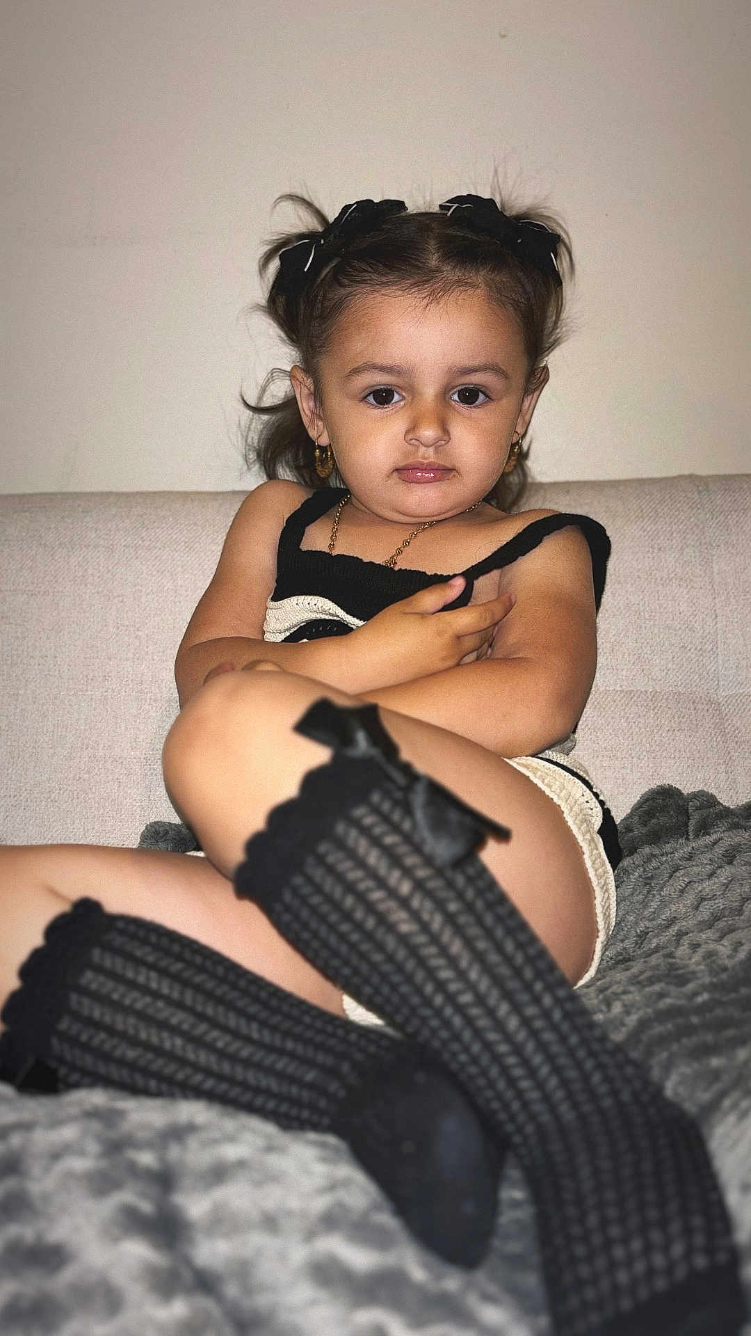 Céliana participe au concours pour gagner de l'argent avec cette photo : child, girl, couch, black_socks, knee_high_socks, bow, earrings, necklace, brown_hair, indoor, blanket, portrait, serious_expression, fashion, knitwear, sitting, young, cute, person, home