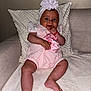baby, infant, pink_outfit, headband, flower, couch, pillow, hand, fingers, smile, sitting, indoor, cute, child, young, person, skin, legs, face, expression