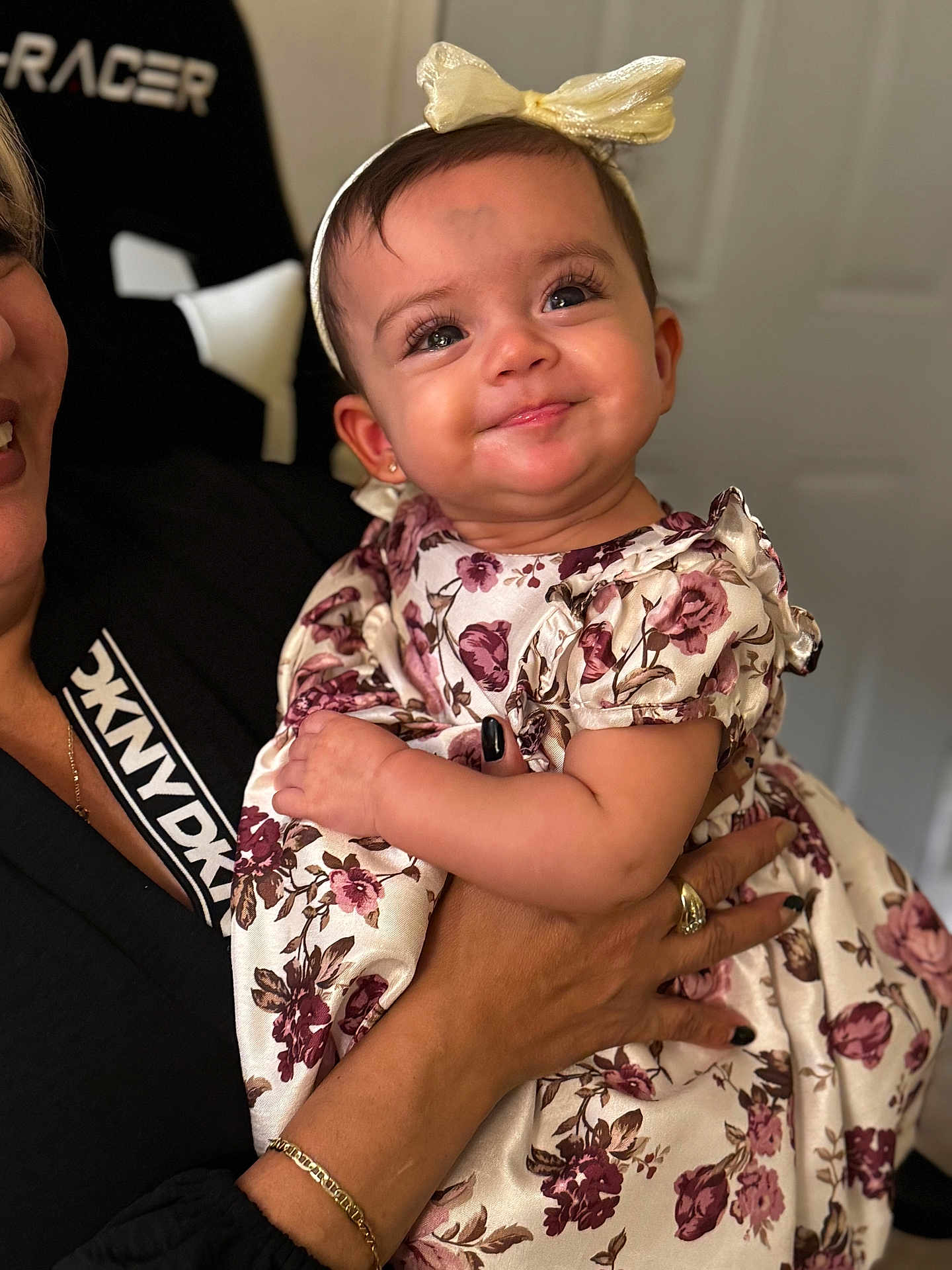 Maddie is registered to the contest to win money with this photo: baby, child, smiling, dress, floral_pattern, headband, bow, hands, adult, portrait, indoor, person, cute, closeup, fashion, skin, face, eyelashes, happy, holding