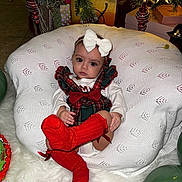 Maddie joined the competition — help win amazing prizes! baby, infant, child, white_bow, red_socks, plaid_dress, cushion, christmas_decorations, ornaments, gift_boxes, holiday, festive, floor, white_blanket, green_balloons, indoor, portrait, cute, seated, holiday_season