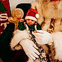 infant, child, santa, beard, santa_hat, gloves, fur_trim, gingerbread, holiday_decor, christmas_sign, green_outfit, chair, indoor, portrait, festive, cozy, smile, baby_pose, seasonal, prop