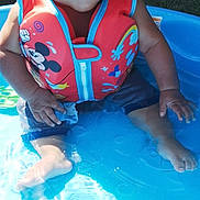 Lisandro Mendez joined the competition — help win amazing prizes! toddler, child, life_jacket, pool, water, sitting, smiling, toy, outdoor, summer, cute, mickey_mouse, playful, wet_hair, blue, red, grass, sunlight, barefoot, happy