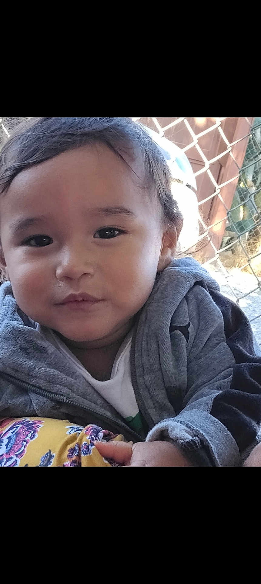 Lisandro Mendez joined the competition — help win amazing prizes! toddler, child, face, portrait, outdoor, jacket, gray_clothing, curly_hair, fence, daylight, person, young_child, casual_clothing, expression, close_up, hand, nature, smile, eye_contact, cute