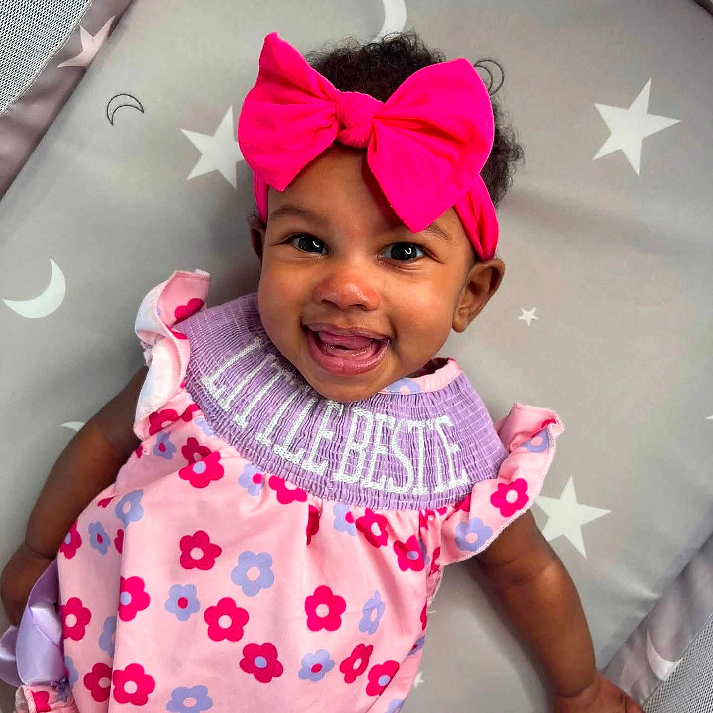 Island joined the competition — help win amazing prizes! baby, child, smiling, pink_bow, floral_dress, headband, infant, happy, cute, lying_down, patterned_mat, stars, moons, indoors, portrait, person, toddler, colorful_clothing, closeup, playpen