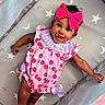 Island is registered to the contest to win money with this photo: baby, child, infant, pink, romper, headband, bow, smile, tongue_out, happy, lying_down, patterned_mat, stars, moons, socks, cute, playful, indoors, person, portrait