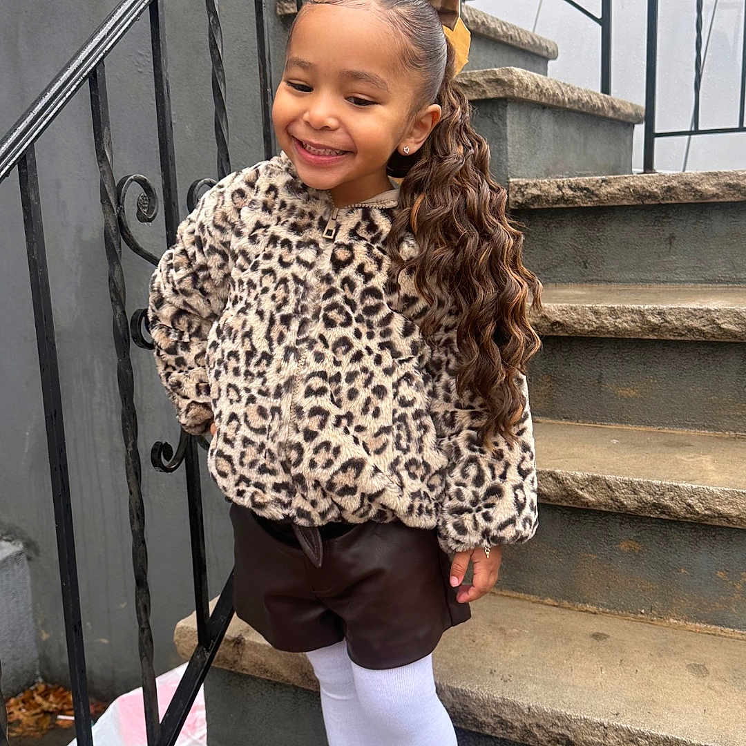 Ailey joined the competition — help win amazing prizes! architecture, building, child, clothing, coat, curlyhair, face, female, footwear, girl, hair, happy, head, house, housing, person, shoe, shorts, sitting, smile